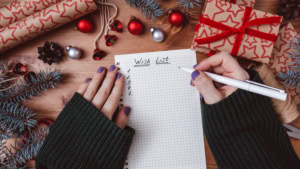 Women's hands write "Wish list" in a notebook
