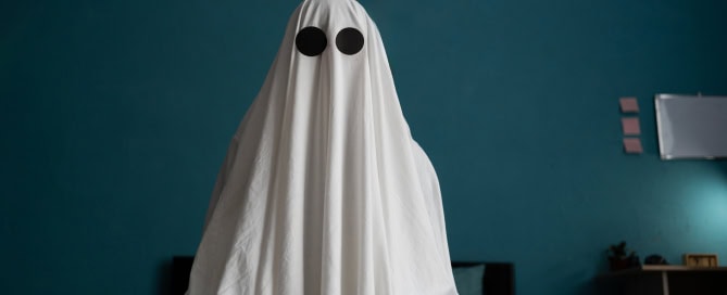 Ghost sitting on the bed at house, close up Halloween concept Man in a white sheet