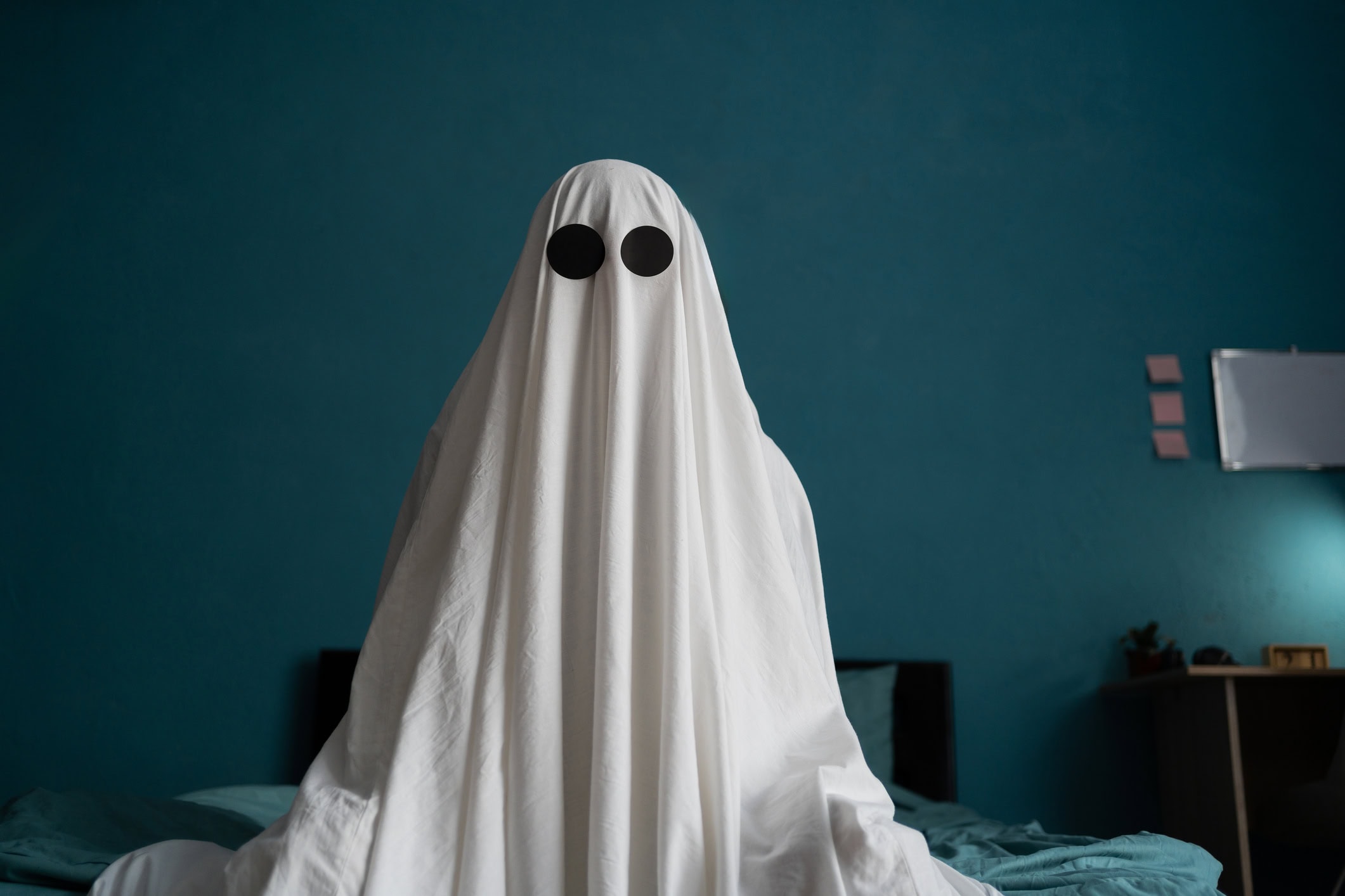Ghost sitting on the bed at house, close up Halloween concept Man in a white sheet