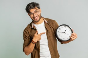 Indian young man showing time hour on wall office clock, ok, thumb up, approve, hurry up, deadline