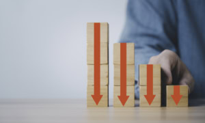 Businessman holding red down arrow which print screen on wooden block cube and copy space for cost profit economy and benefit decreasing concept